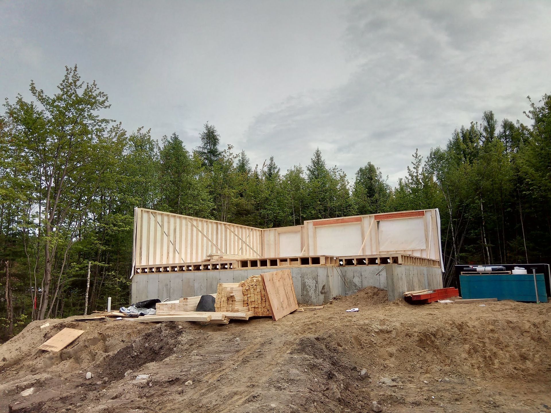 Une maison est en construction au sommet d’une colline de terre entourée d’arbres.