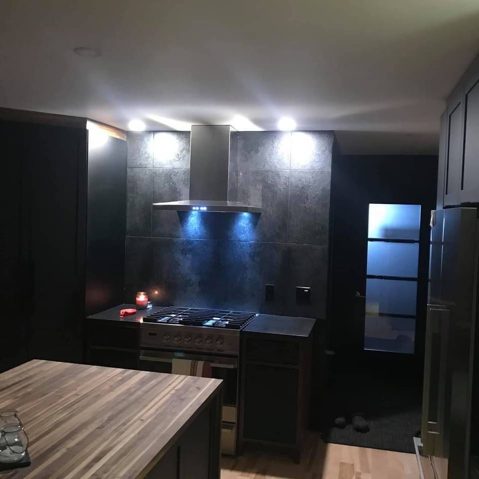 Cuisine avec armoires foncées, dosseret gris, hotte en acier inoxydable et îlot en bois.