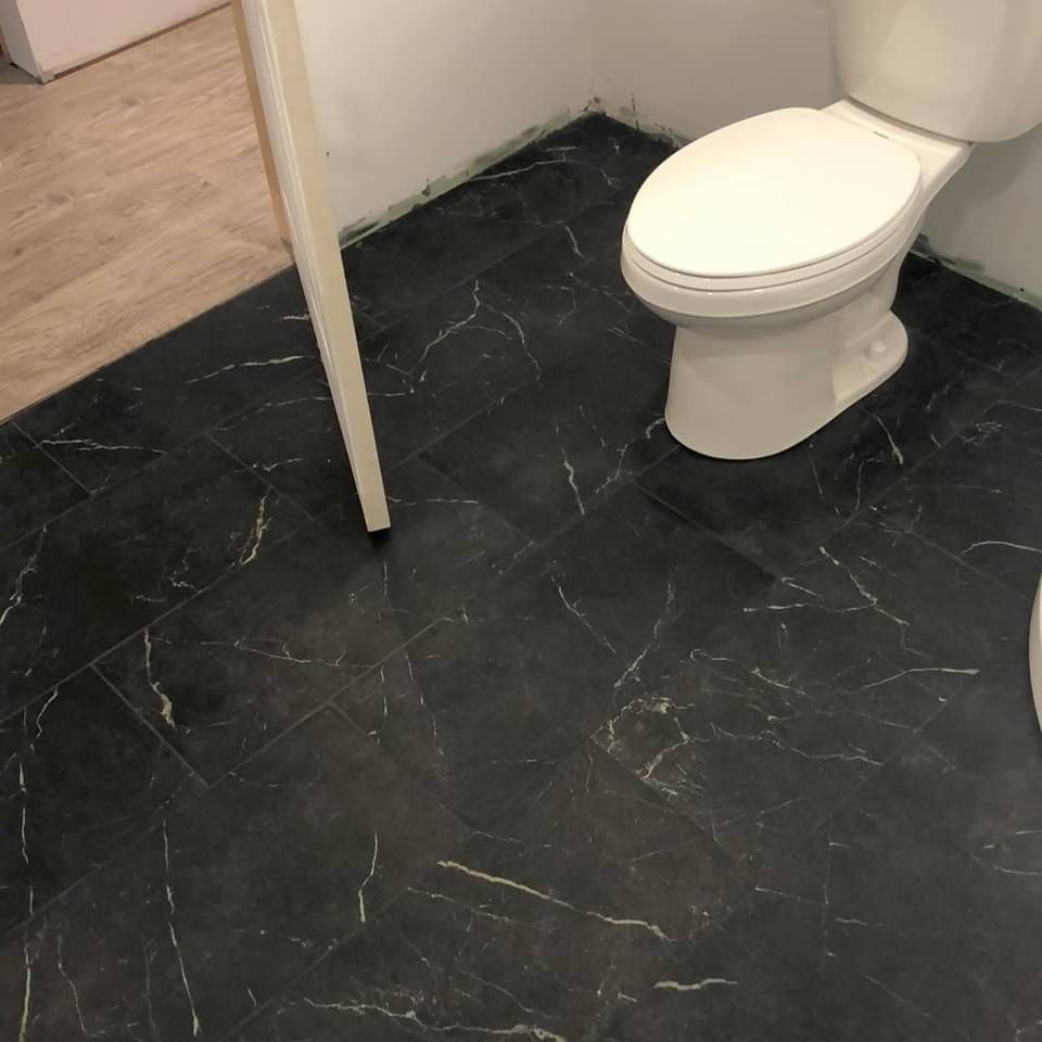 Des toilettes sont posées sur un sol carrelé noir dans une salle de bains