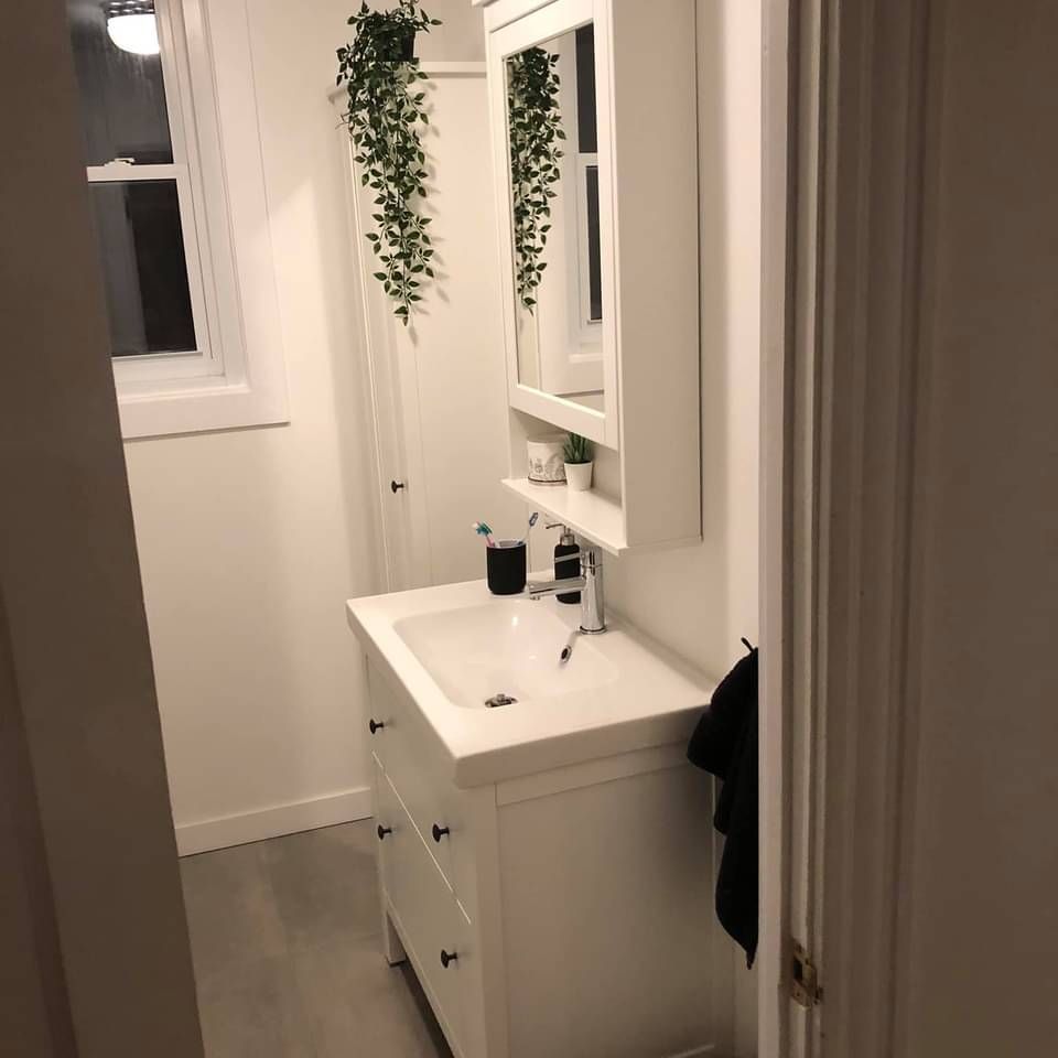 Salle de bain blanche avec lavabo, miroir et plantes suspendues.