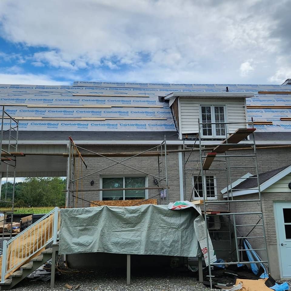 Une maison est en cours de rénovation avec des échafaudages et une bâche sur le toit.