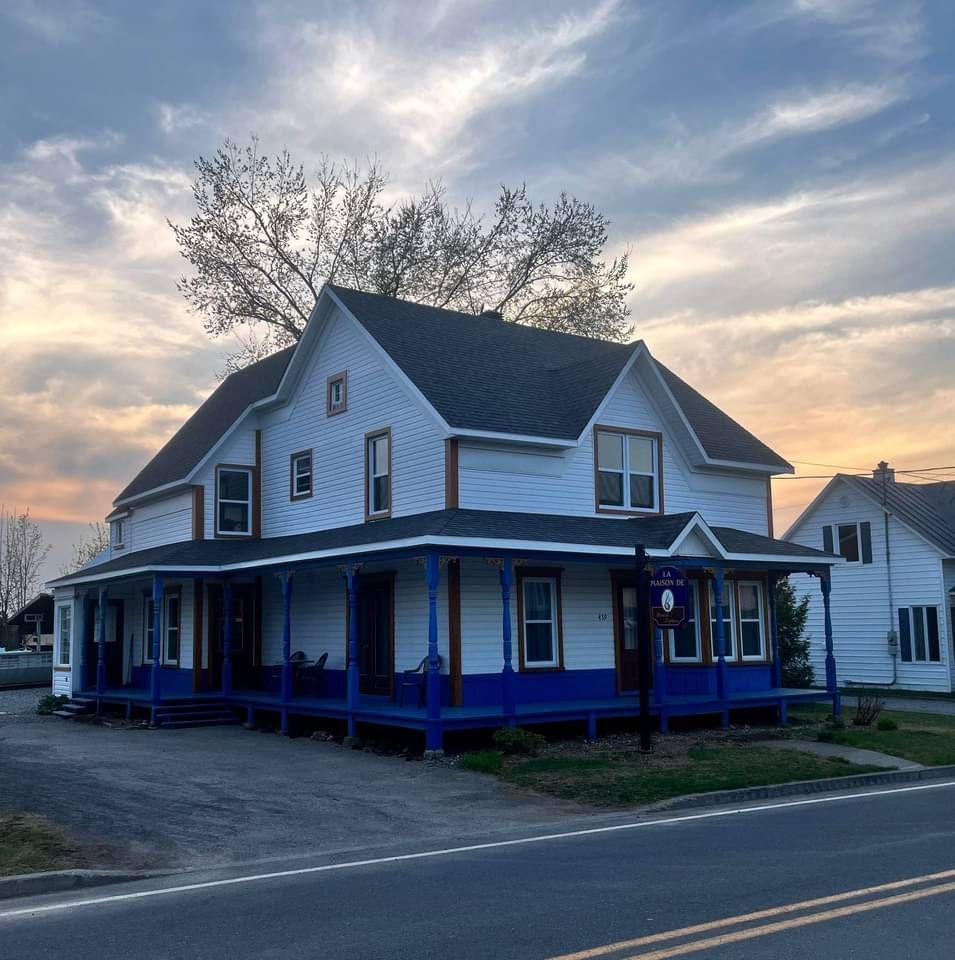 Une maison blanche avec un porche bleu et un coucher de soleil en arrière-plan