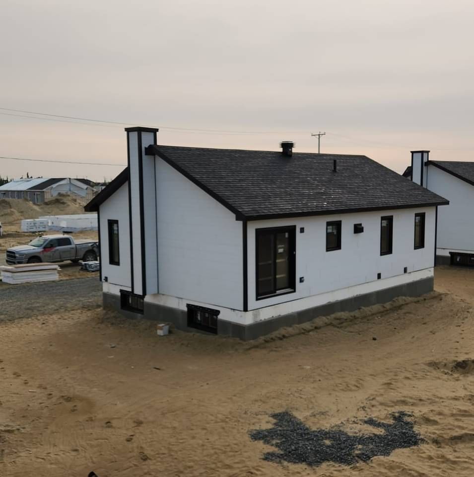 Une maison blanche avec un toit noir se trouve au milieu d'un champ de terre