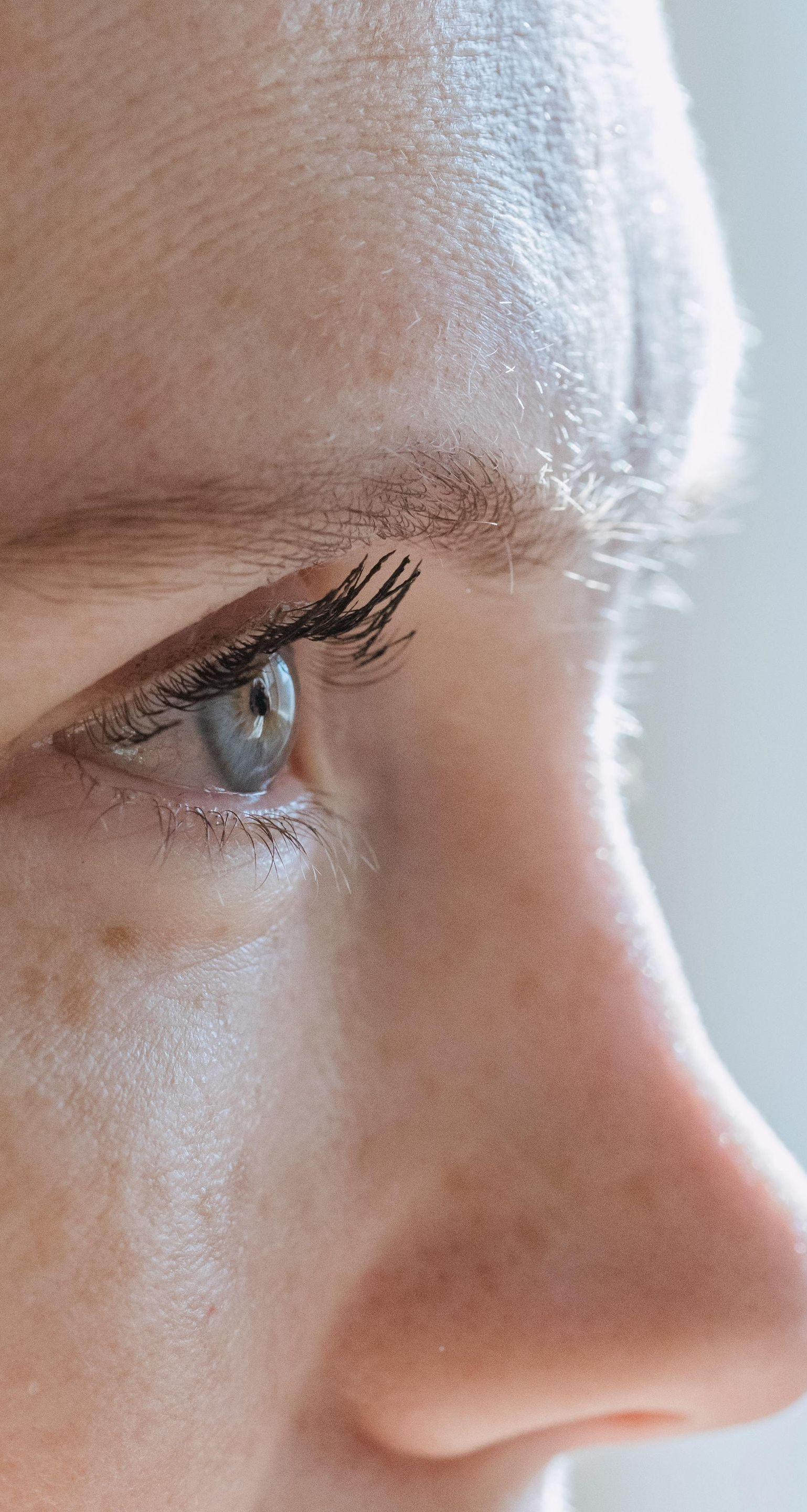 Close-up of a person's eye and nose; fair skin, light-colored eye with mascara, side profile view.