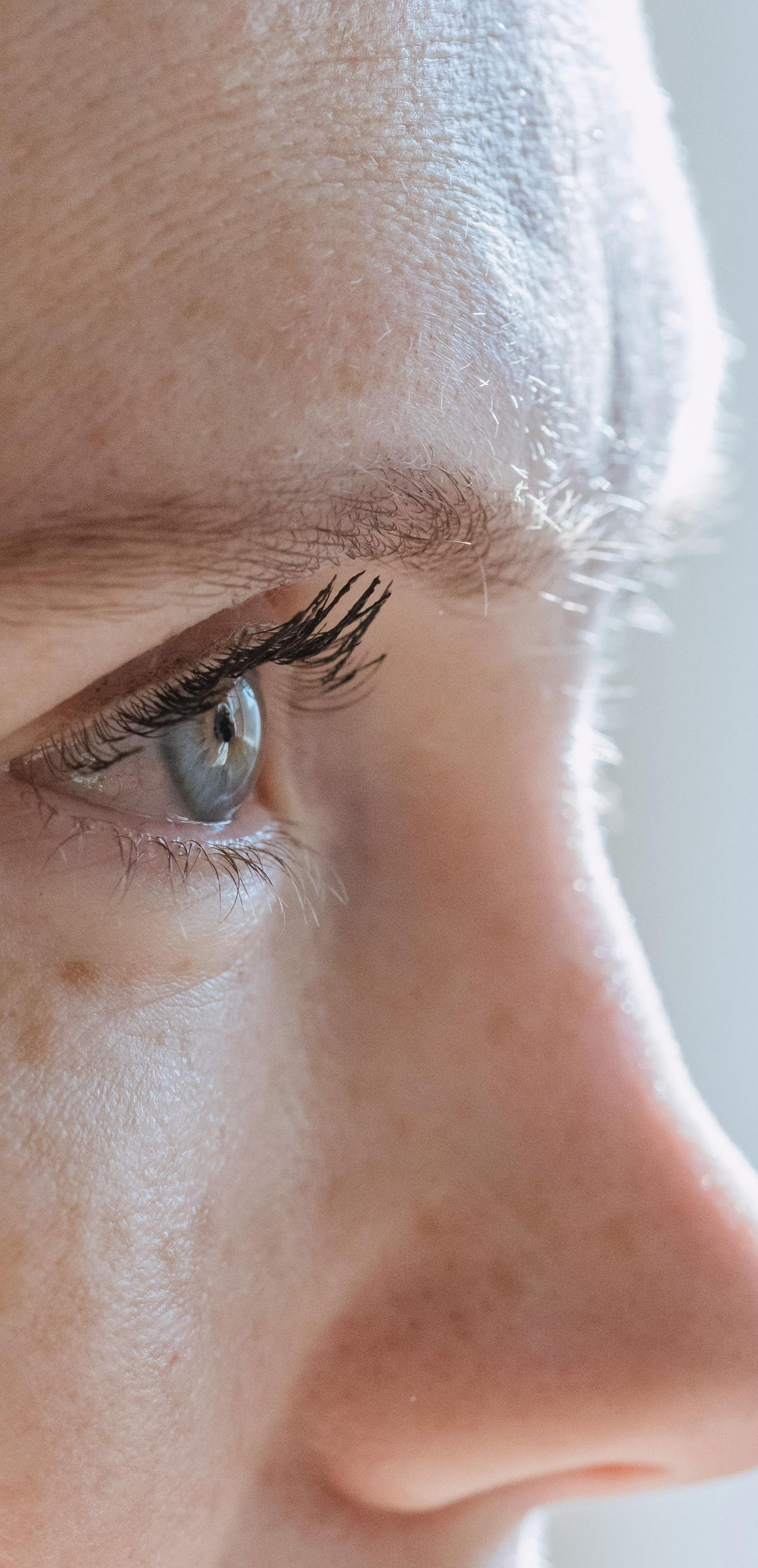 Close-up of a person's eye and nose; fair skin, light-colored eye with mascara, side profile view.