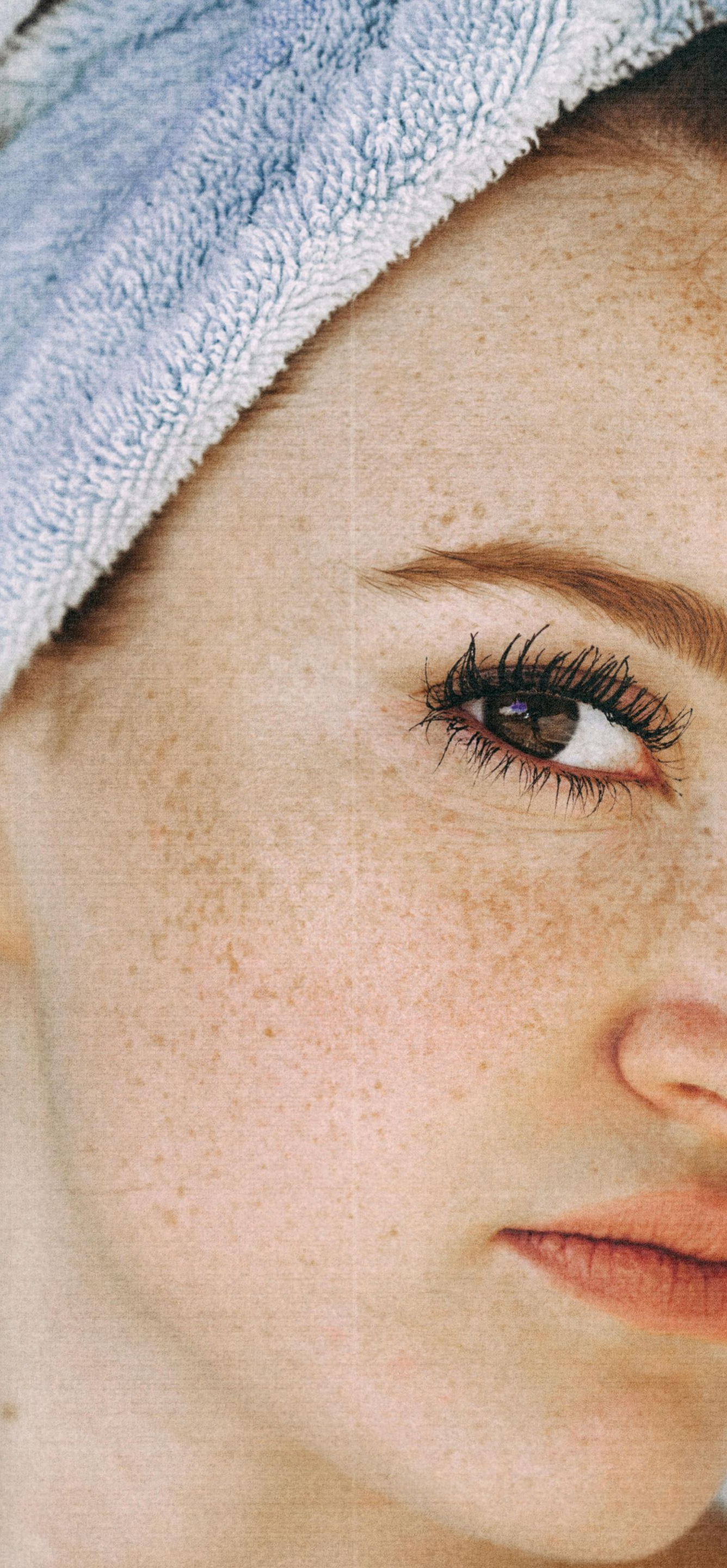 Woman with freckled skin, wrapped in a light blue towel, looking down.