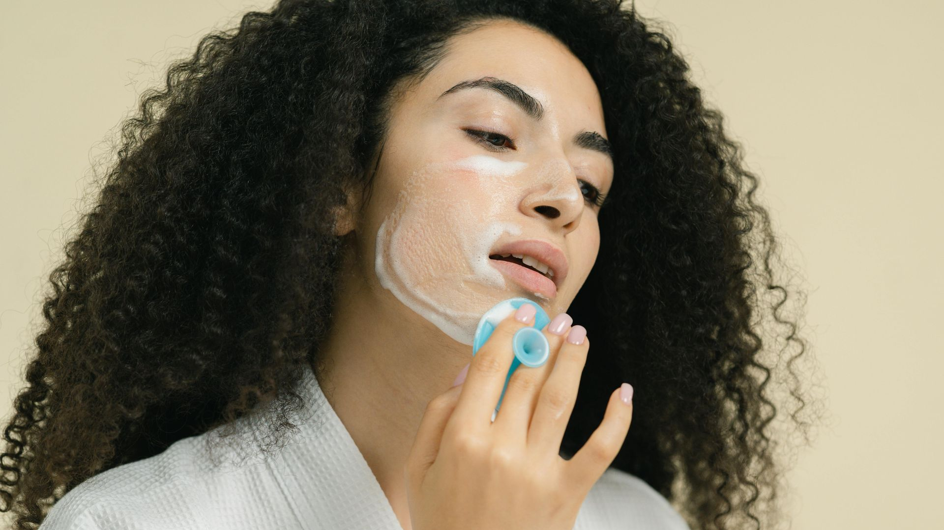 Woman in a robe using a blue facial cleansing tool on her face.