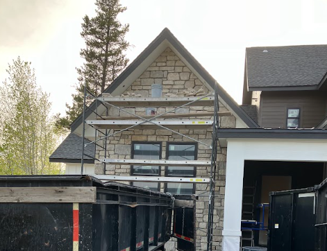 Construction site with stone facade, scaffolding, and a dumpster in front of a house.