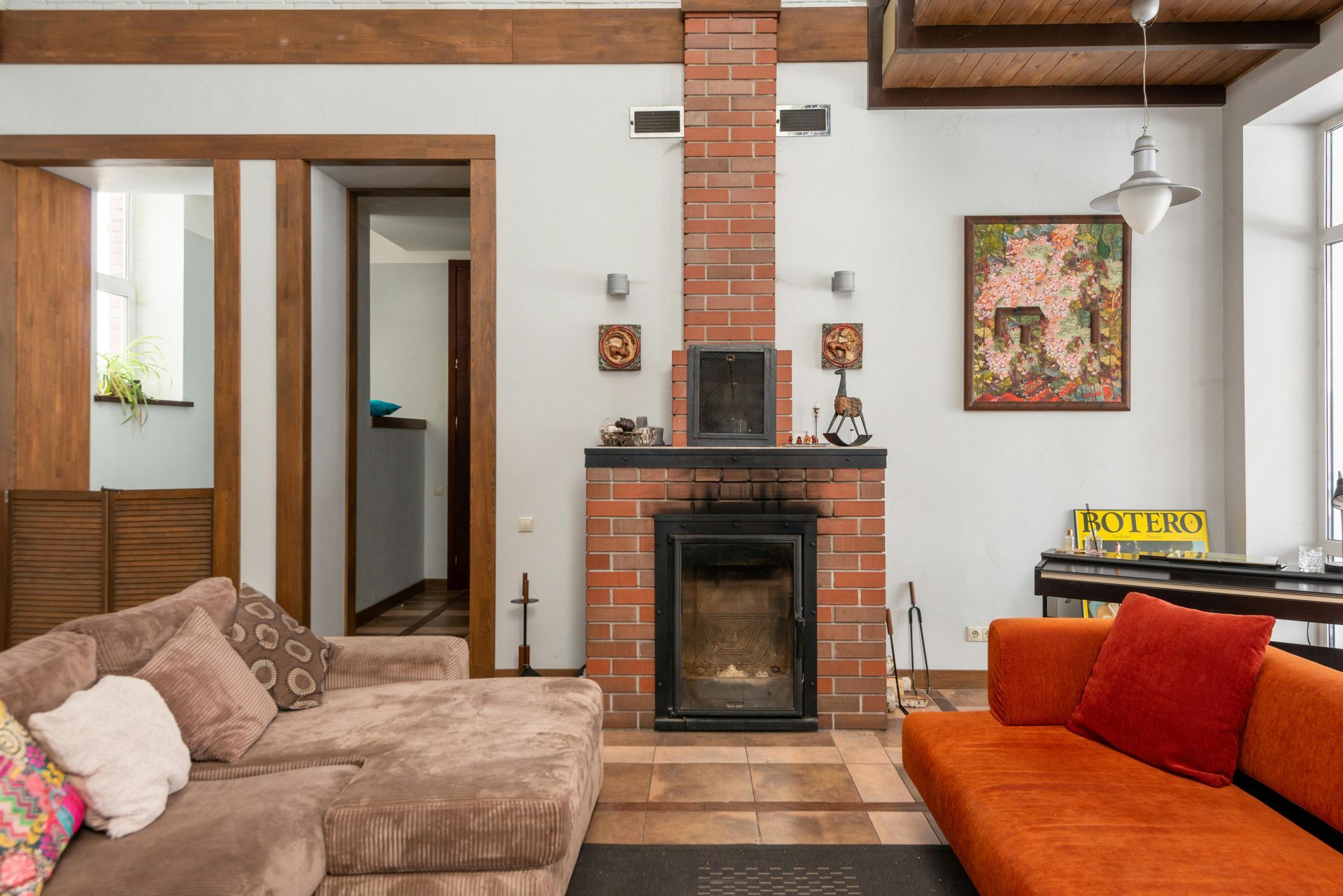 Living room with brick fireplace, brown and orange sofas, and artwork.