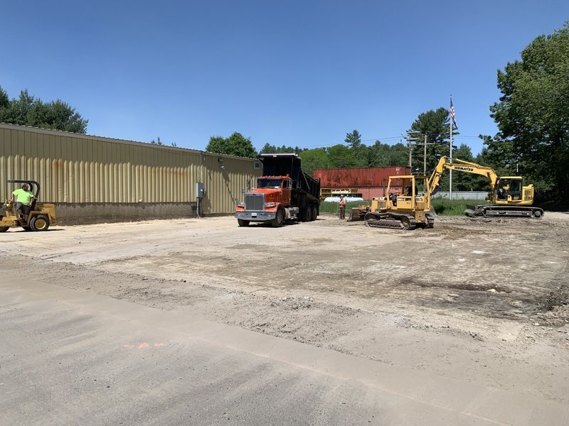 A dump truck is parked in a dirt lot next to a forklift