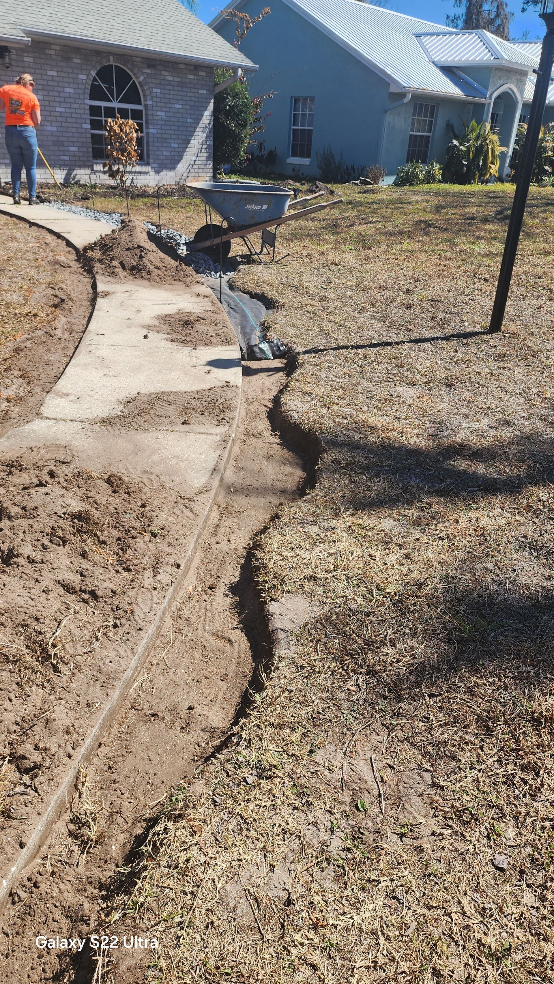 Cracked concrete walkway beside a gravel yard and blue house under construction, with workers in the background