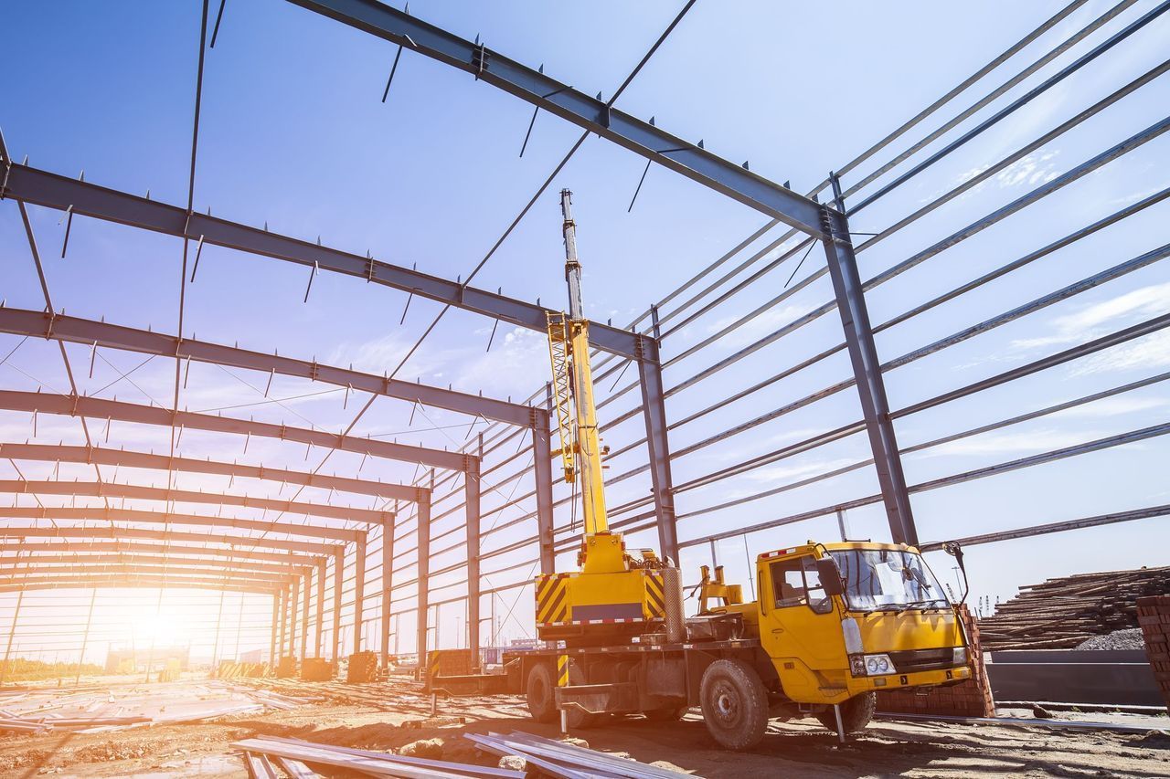 Yellow crane assembling steel beams at a construction site; bright sunlight.