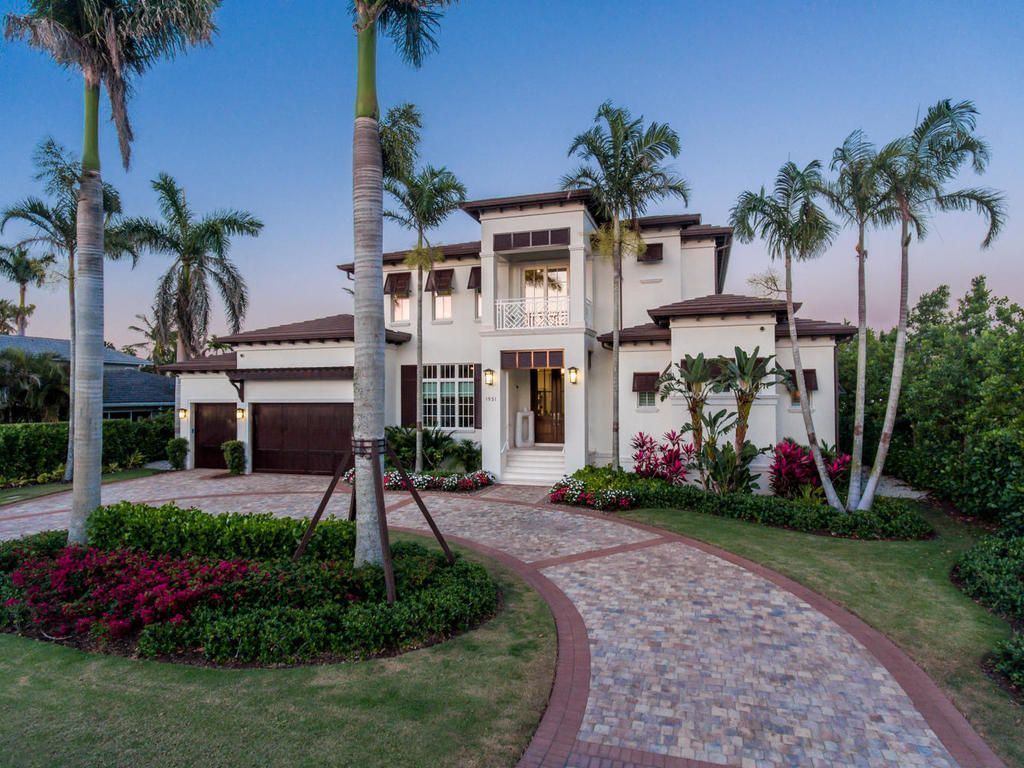 Large white house with brown accents, palm trees, and a stone driveway.