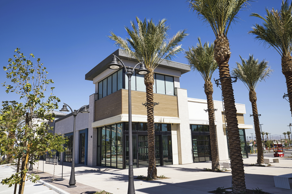 Modern building with palm trees on a sunny day. White walls, large windows, and grey roof.
