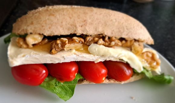 Sandwich met tomaat, sla, brie, honing en walnoten in een volkorenbroodje, geserveerd op een bord.