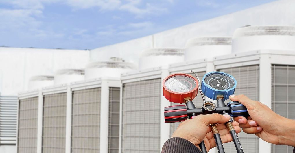Person using gauges to service an air conditioning unit on a building rooftop.