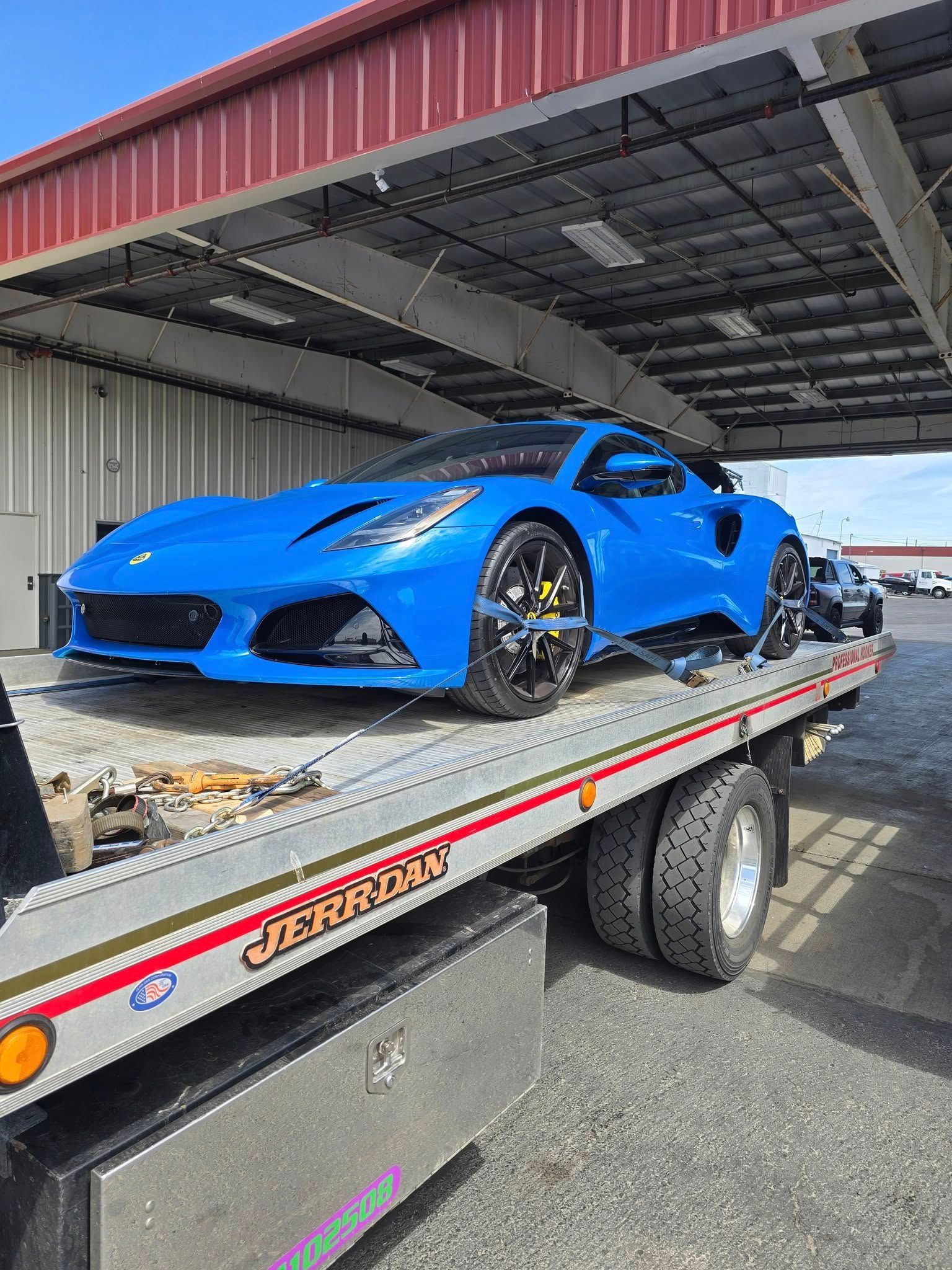 Blue sports car on a tow truck, under a red awning.