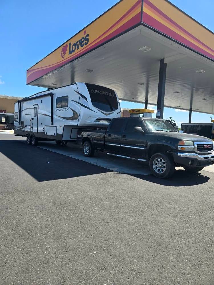 Truck towing a fifth-wheel RV at a Love's gas station under a canopy with the Love's logo.