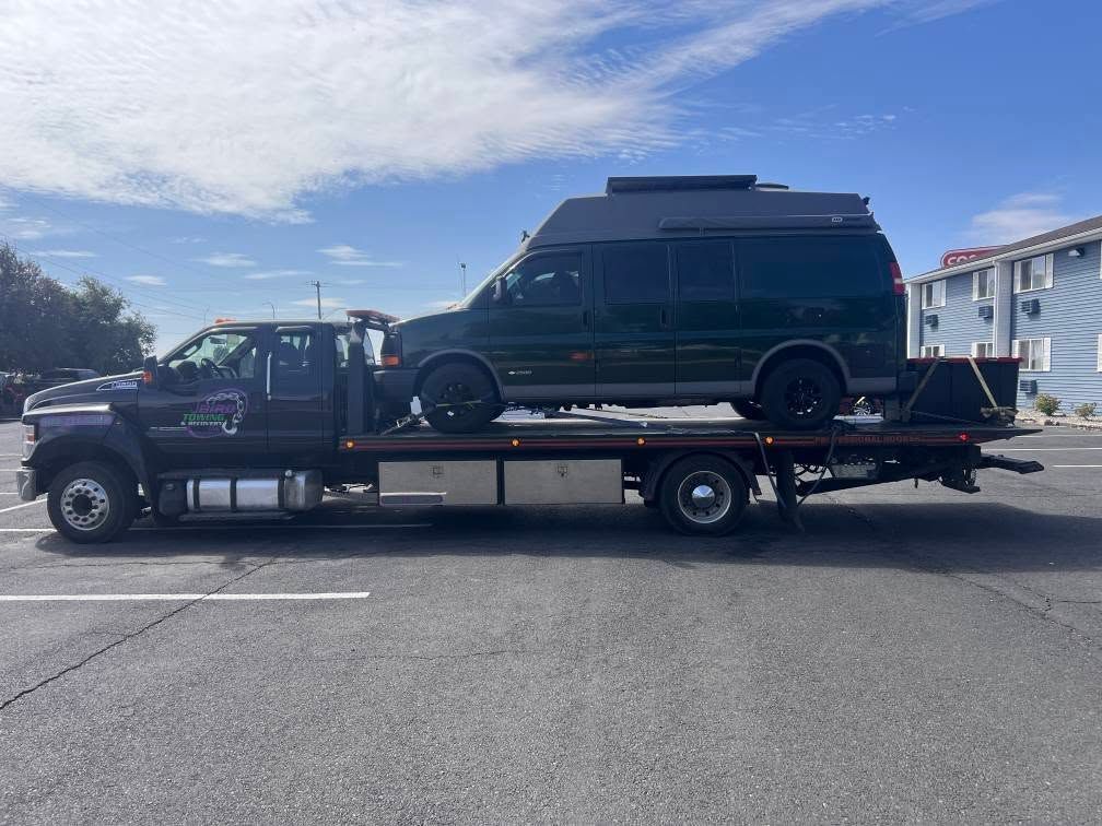 Dark green van loaded onto a flatbed tow truck on a sunny day.