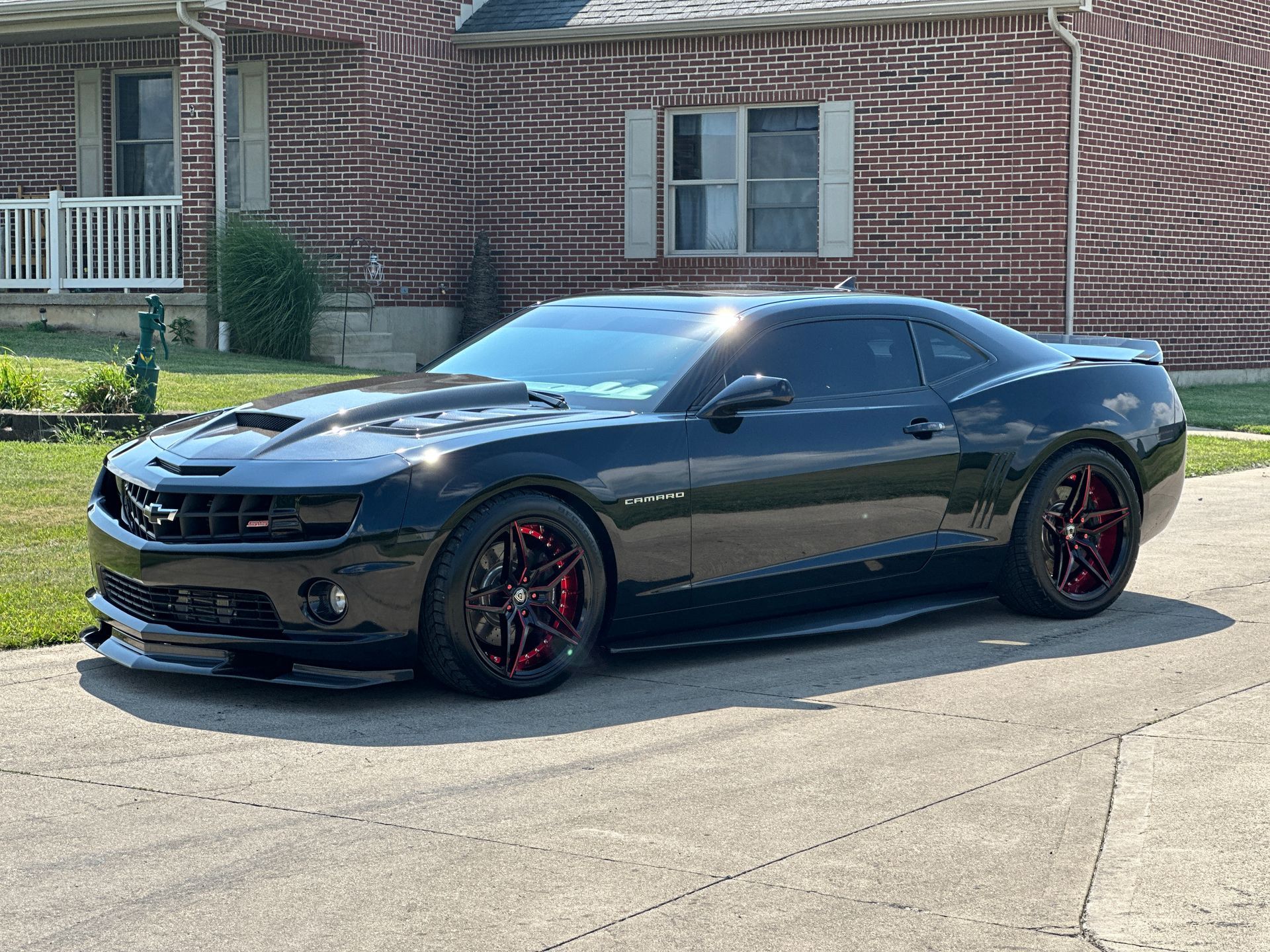 A black car is parked in front of a brick house.