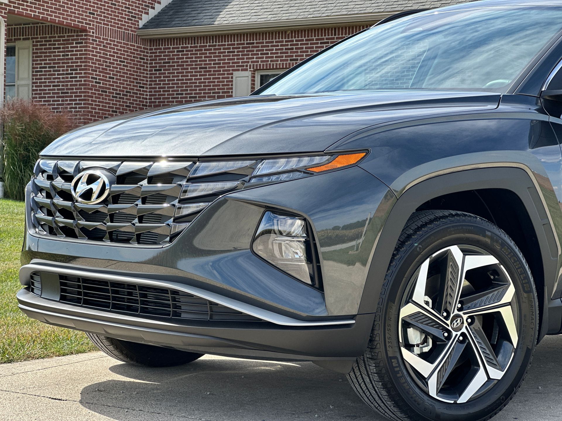 A black hyundai tucson is parked in front of a brick house.