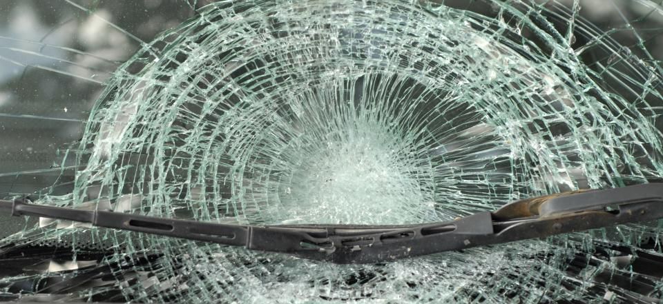 Cracked car windshield with wiper visible, damaged glass showing extensive cracking from impact.