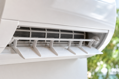 Close-up of a white air conditioner vent with adjustable louvers indoors