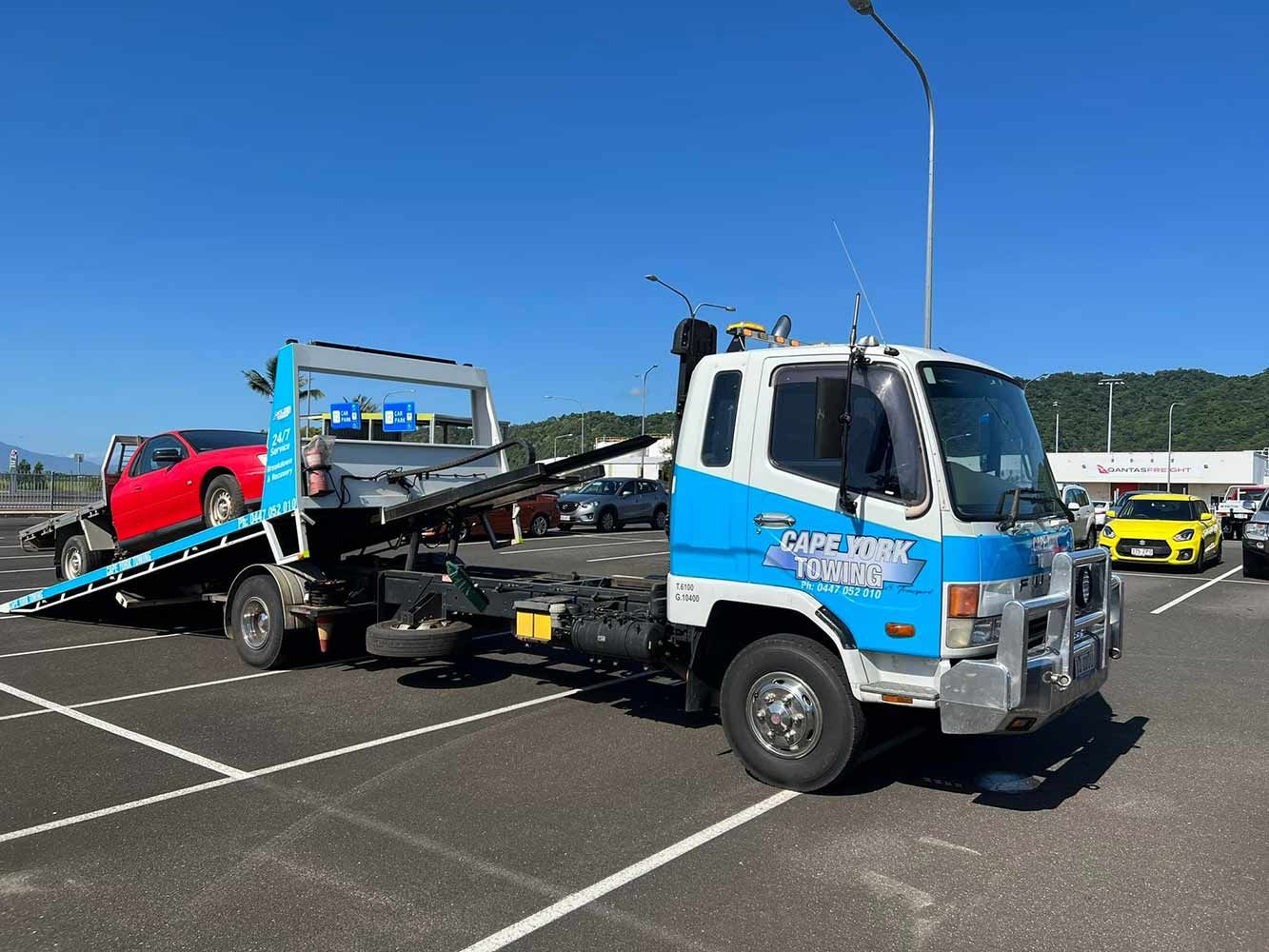 A Tow Truck is Towing a Red Car in a Parking Lot — Cape York Towing & Transport in Weipa, QLD