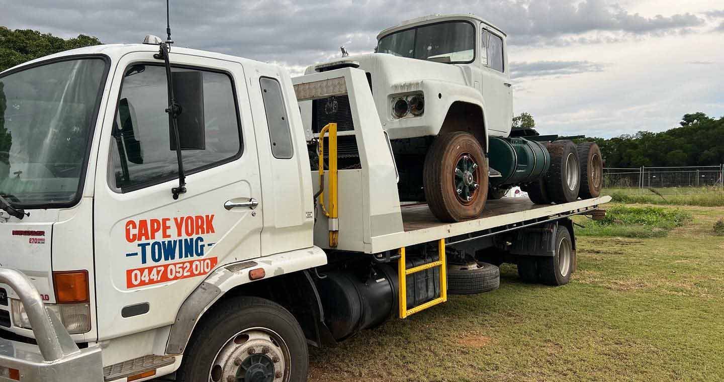 A White Tow Truck With Two Cars on the Back is Parked in a Field — Cape York Towing & Transport in Weipa, QLD