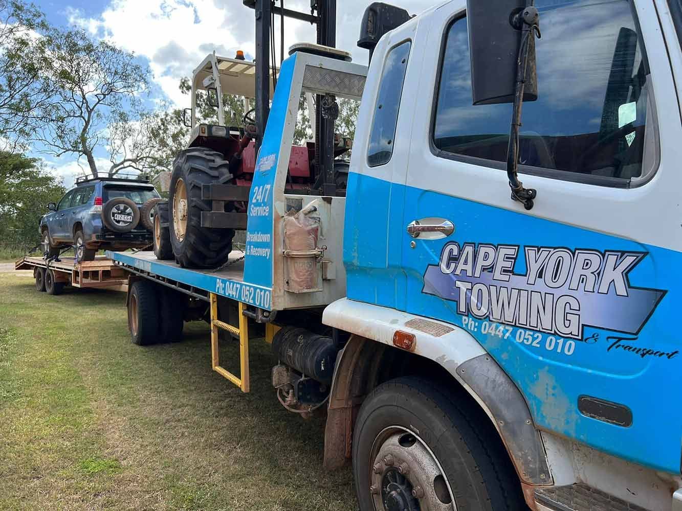 A Blue and White Towing Truck is Carrying a Tractor and a Car — Cape York Towing & Transport in Mareeba, QLD