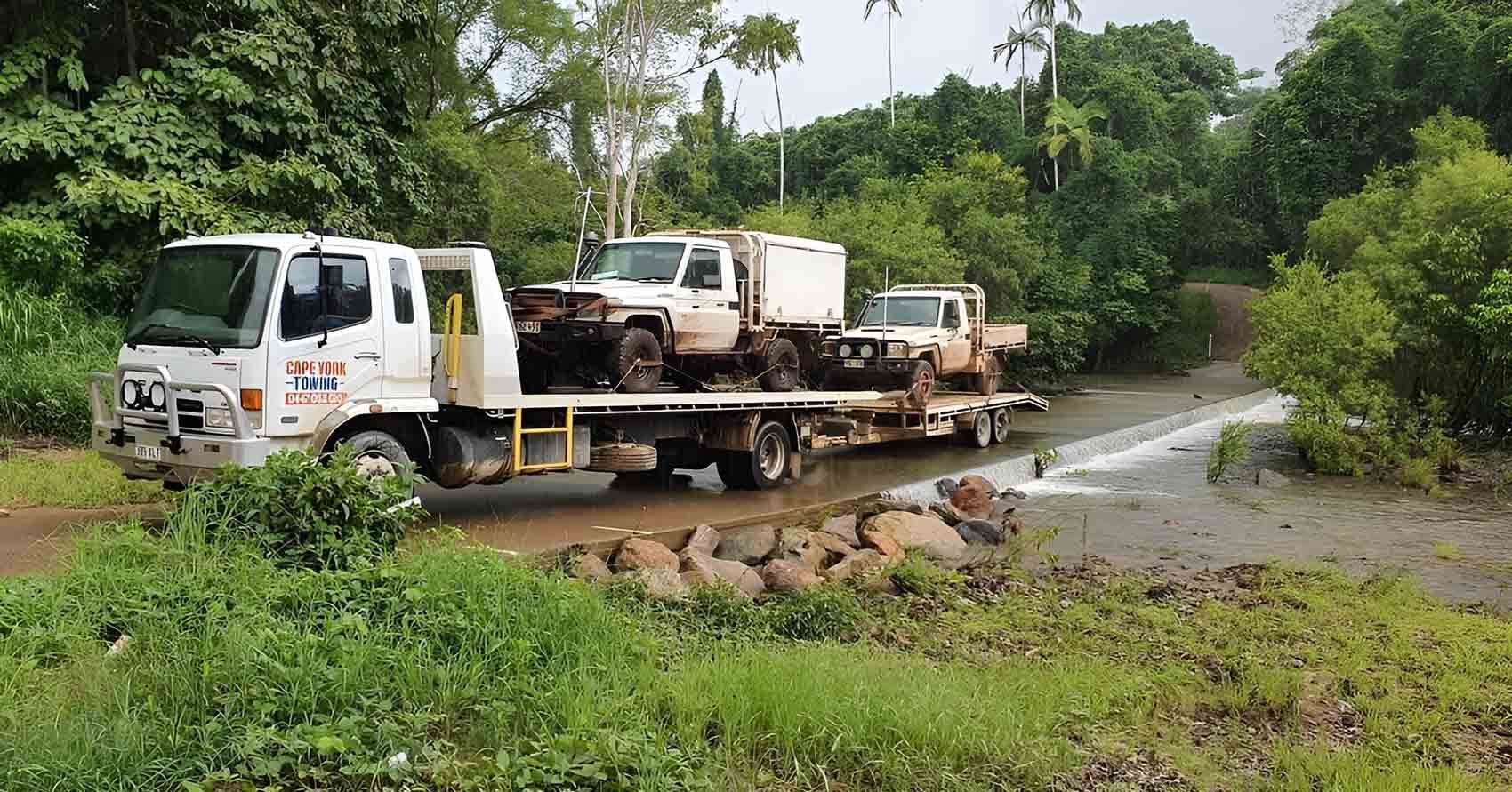A Tow Truck is Carrying Two Trucks Down a Muddy Road — Cape York Towing & Transport in Cape York, QLD