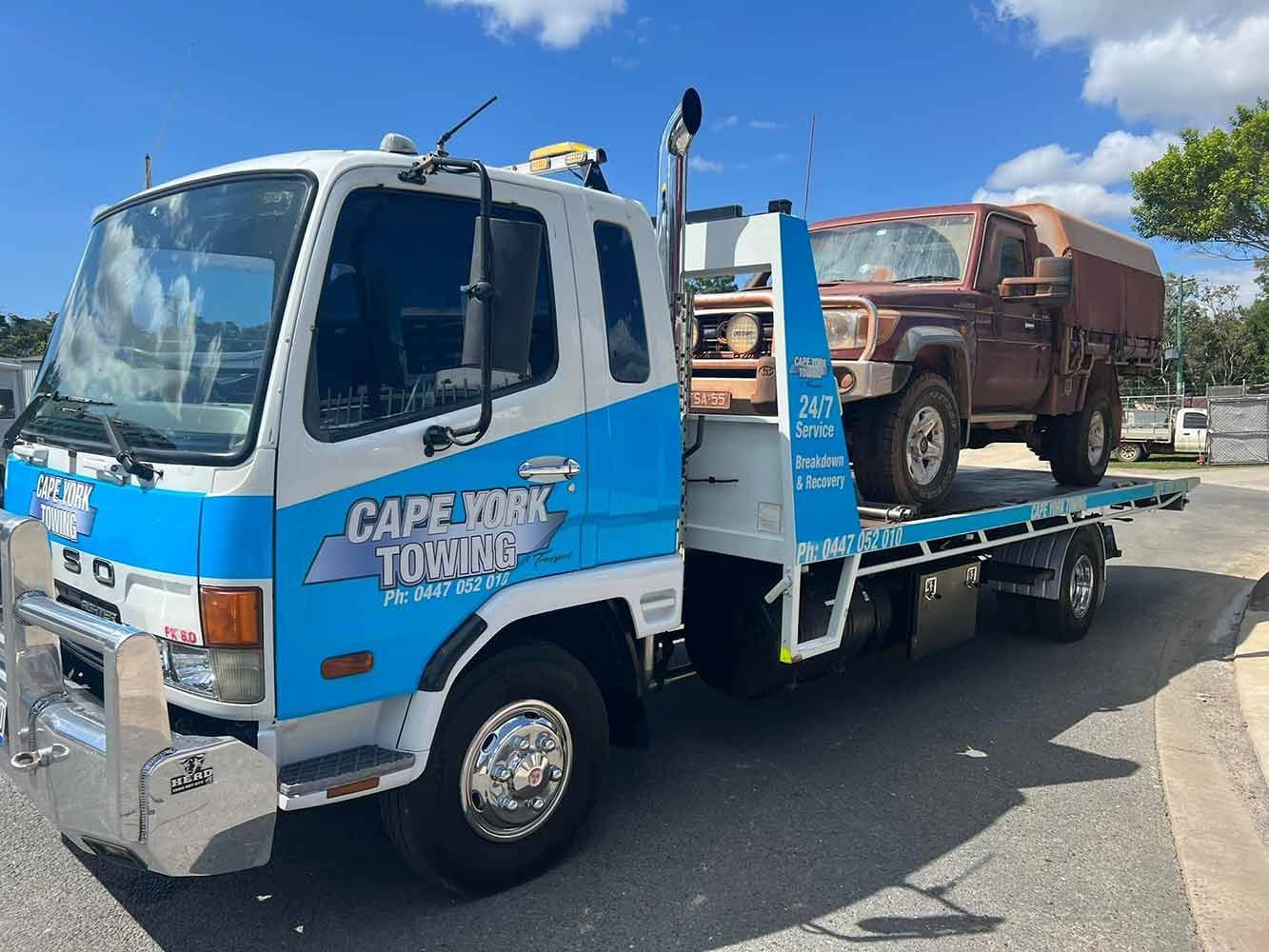 A Blue and White Tow Truck With a Red Truck on the Back is Parked on the Side of the Road — Cape York Towing & Transport in Croydon, QLD