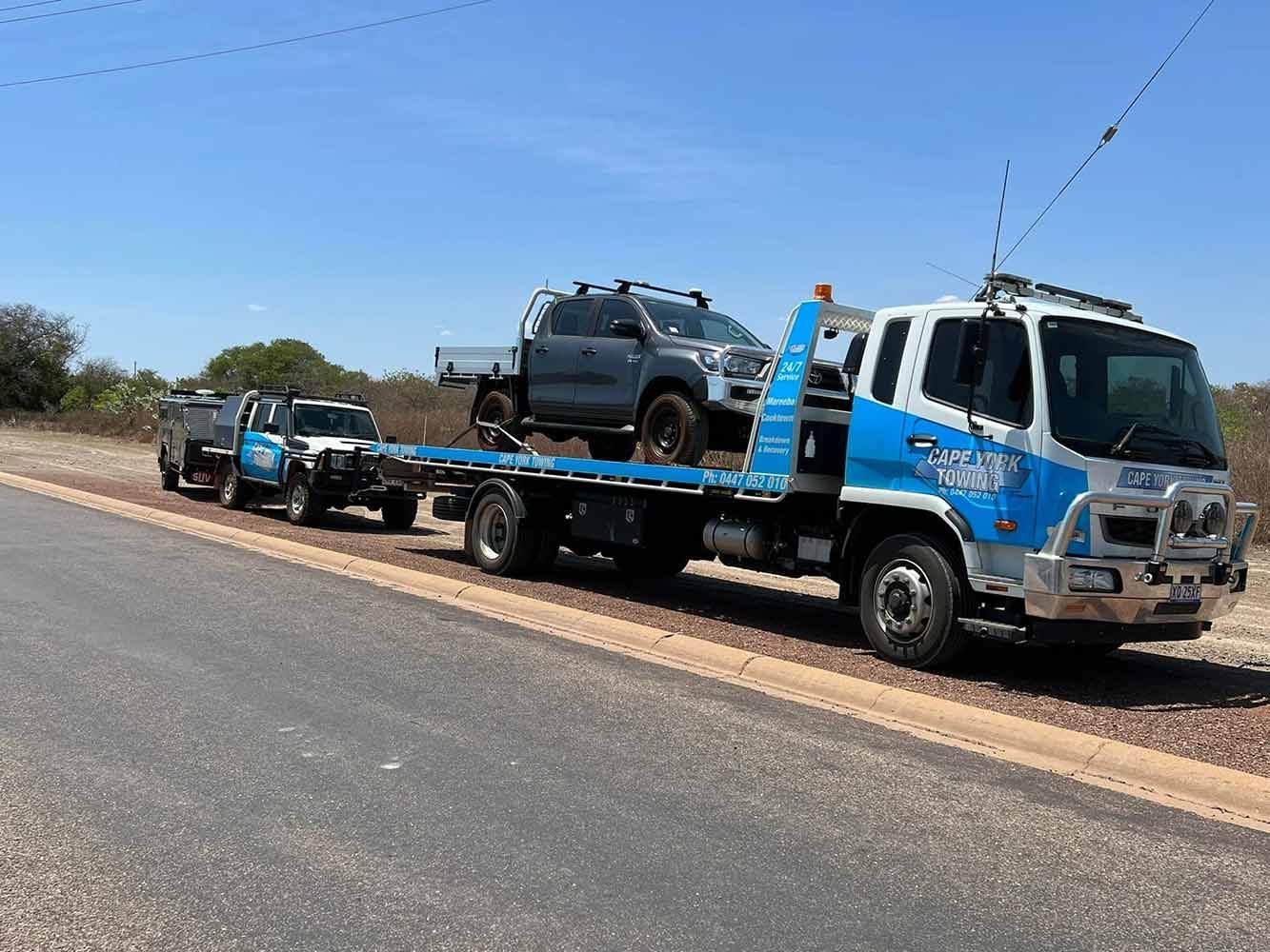 A Tow Truck is Carrying a Row of Trucks Down a Road — Cape York Towing & Transport in Bramwell, QLD