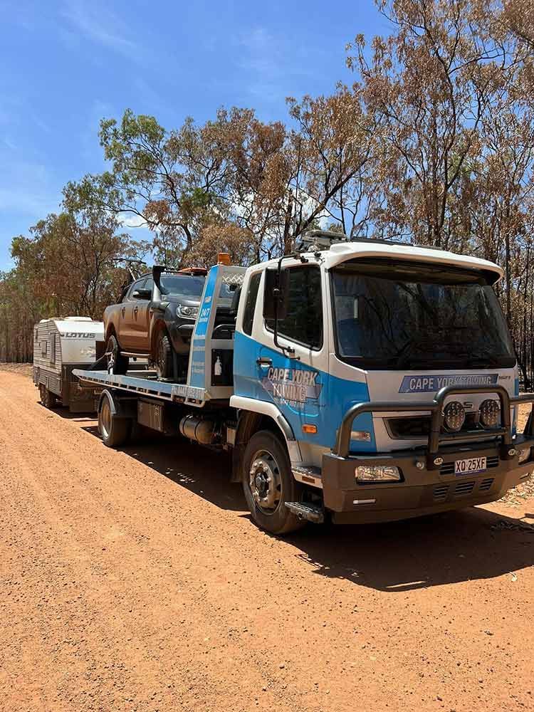 A Tow Truck is Carrying a Car and a Trailer on a Dirt Road — Cape York Towing & Transport in Seisia, QLD