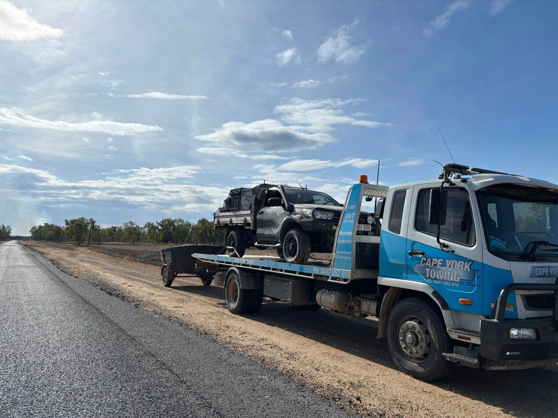 A Tow Truck With a Black Pickup Truck on Its Flatbed Parked on the Side of a Rural Road Under a Cloudy Sky — Cape York Towing & Transport in Cairns, QLD