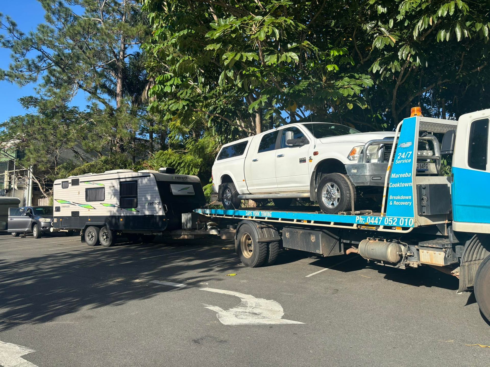 A White Truck on a Tow Truck With a Camper Trailer Hitched to It, Parked on Asphalt — Cape York Towing & Transport in Cairns, QLD