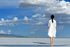 A woman in a white dress is standing on a lake looking at the clouds.