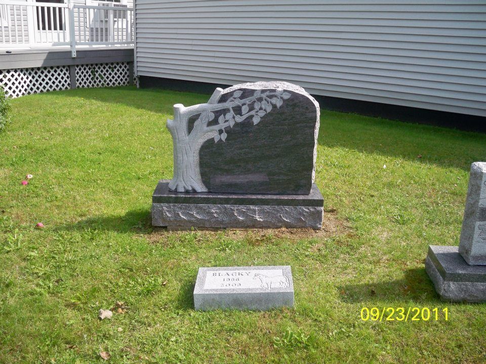 Headstone with tree carving, on a grassy lawn, beside a small rectangular stone.