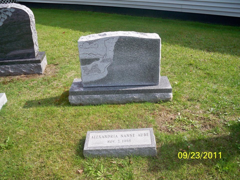 Tombstone for Alexandria Kane, gray stone with inscription, set in grass.