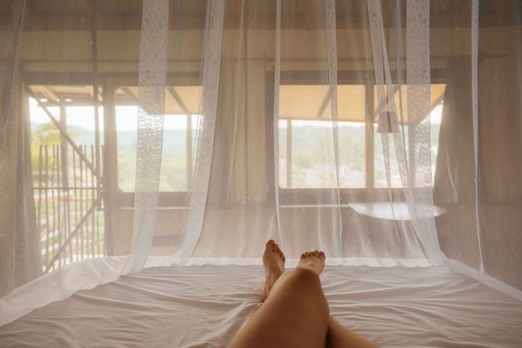 Una mujer está acostada en una cama debajo de un mosquitero. Vistas increibles , Mazunte, Posada del Arquitecto.