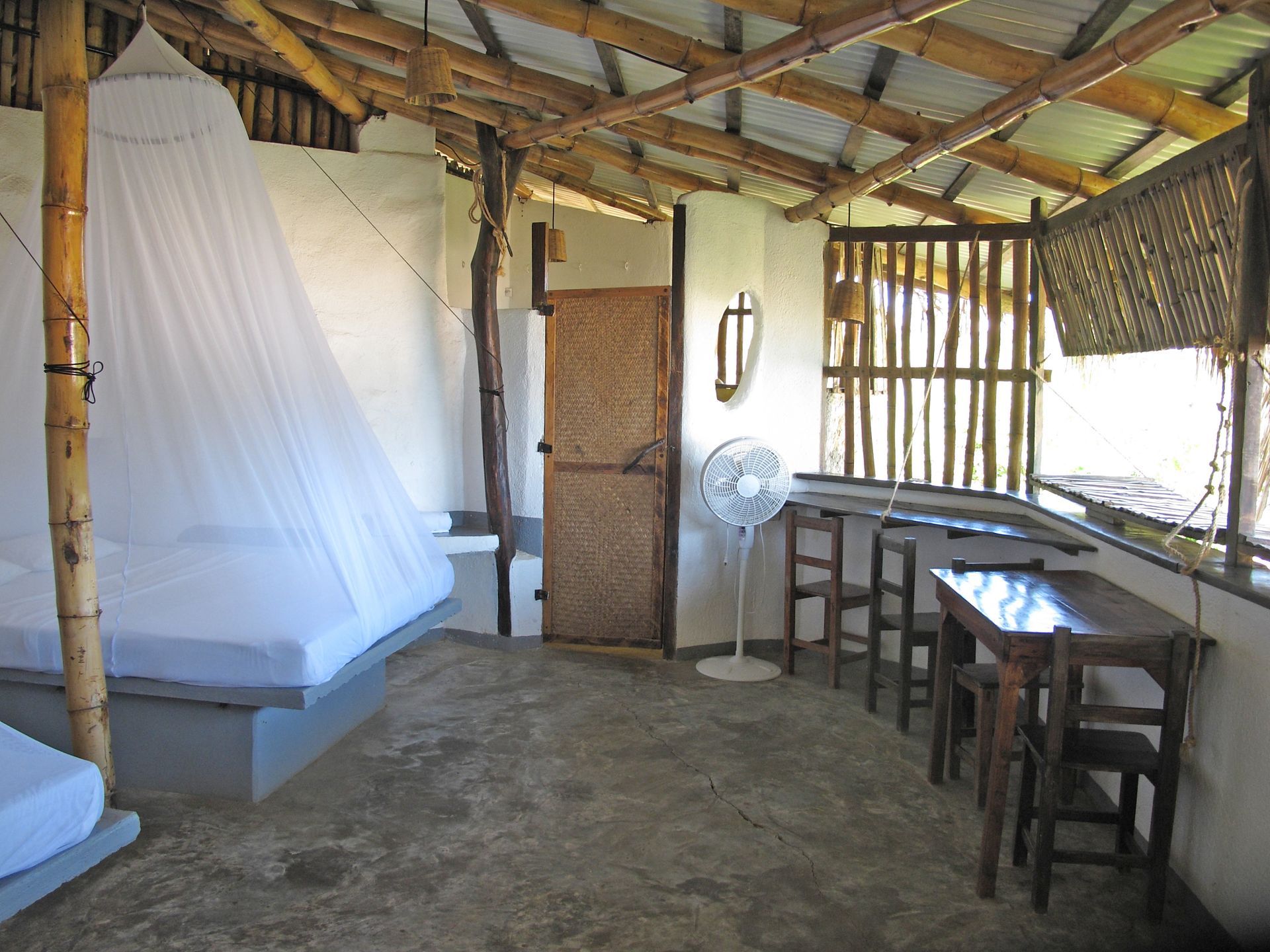 Interior de una habitación sencilla con camas, una mesa y paredes abiertas hechas de bambú en posada del arquitecto