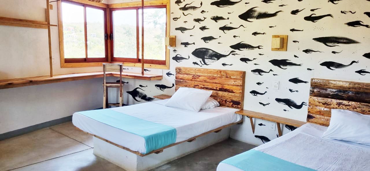 Una habitación con dos camas individuales y una ventana grande en posada del arquitecto en mazunte, oaxaca
