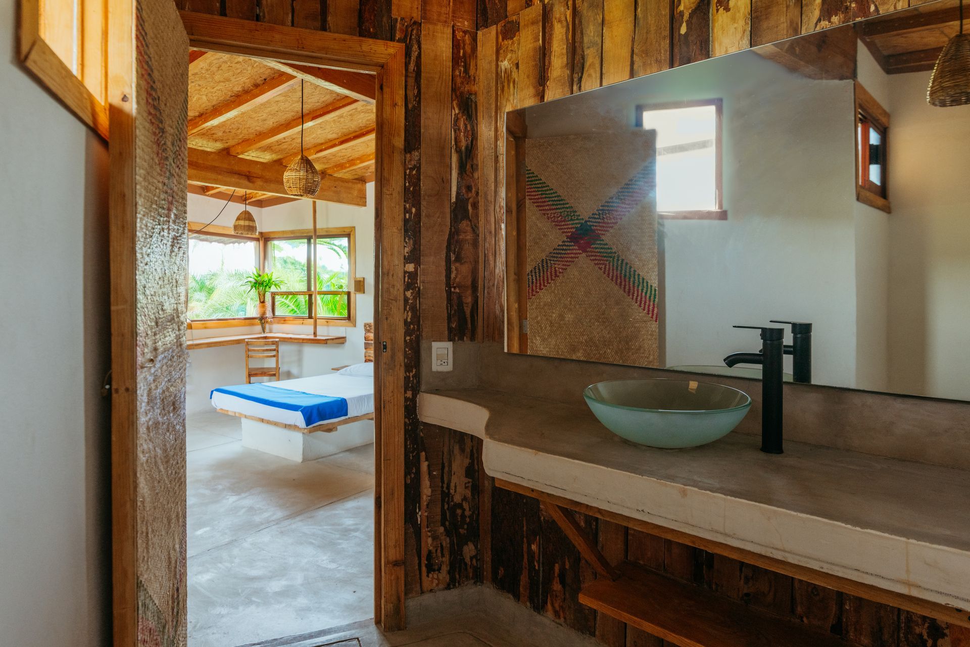 Baño con paredes rústicas de madera y vistas a un dormitorio con cama en posada del arquitecto en mazunte, oaxaca
