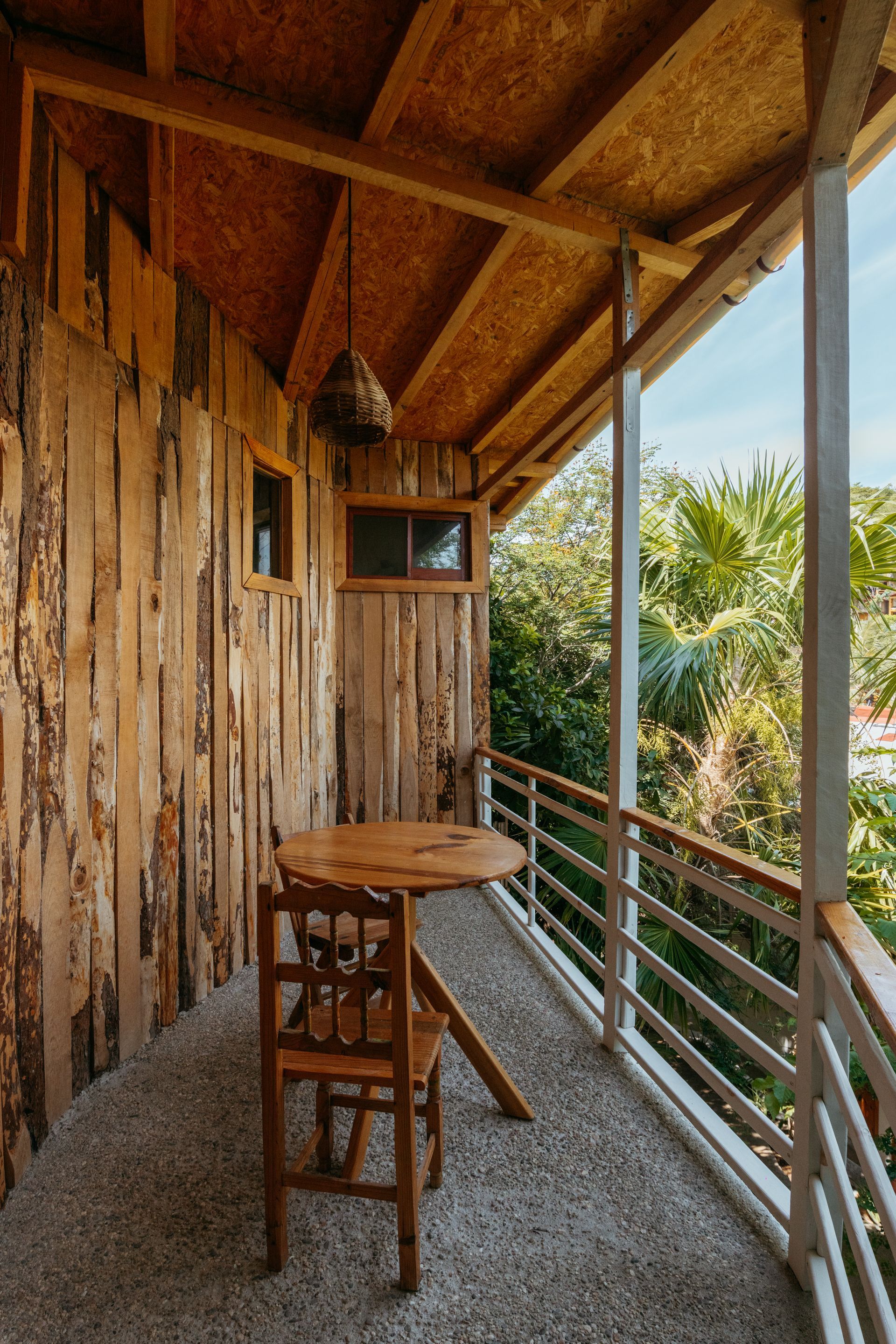 Balcón de madera con mesa y silla, con vistas a la vegetación en posada del arquitecto en mazunte, oaxaca