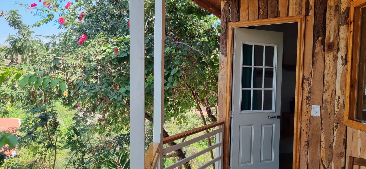 Entrada de una cabaña con balcón con vistas a árboles y flores en posada del arquitecto en mazunte, oaxaca