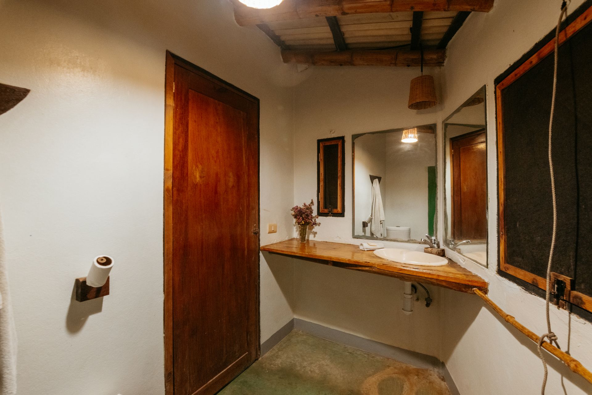 Baño con puerta de madera, lavabo, espejo y suelo de hormigón en posada del arquitecto