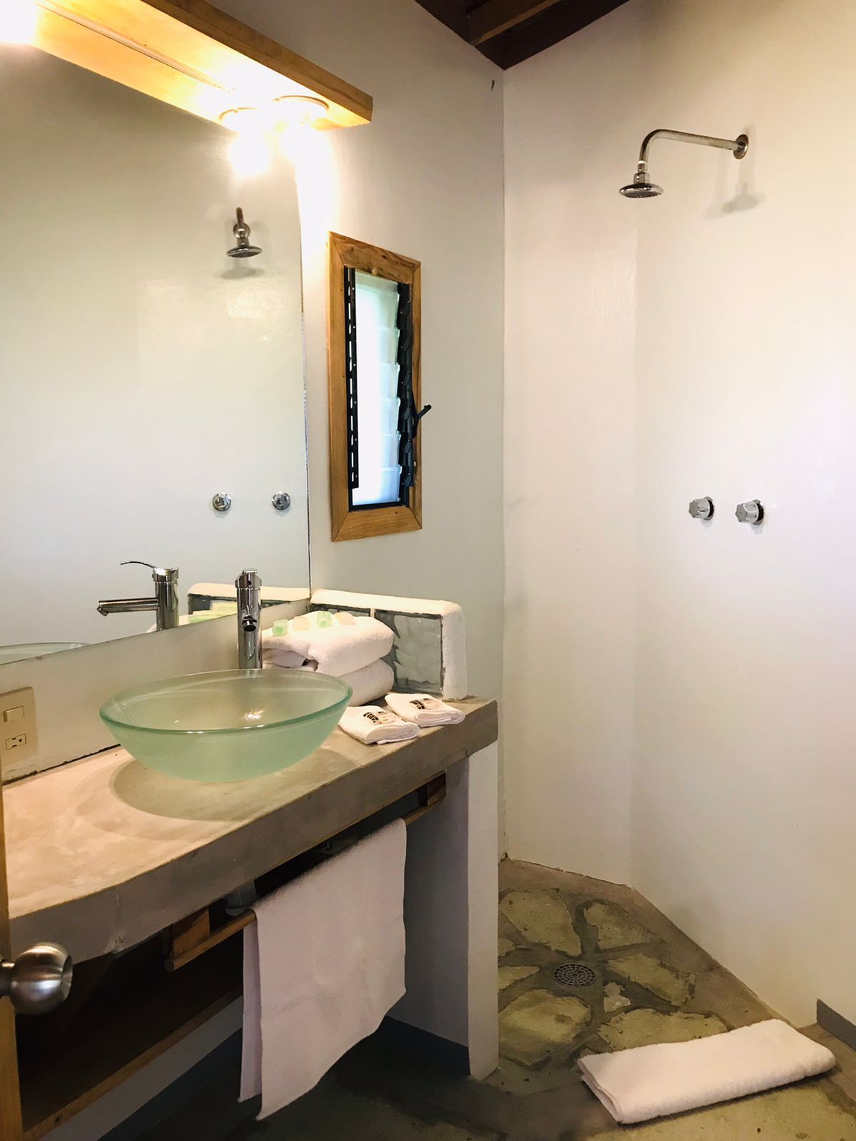 Baño con lavabo de cristal, ducha, toallas y ventana con contraventanas abiertas en posada del arquitecto en mazunte, oaxaca