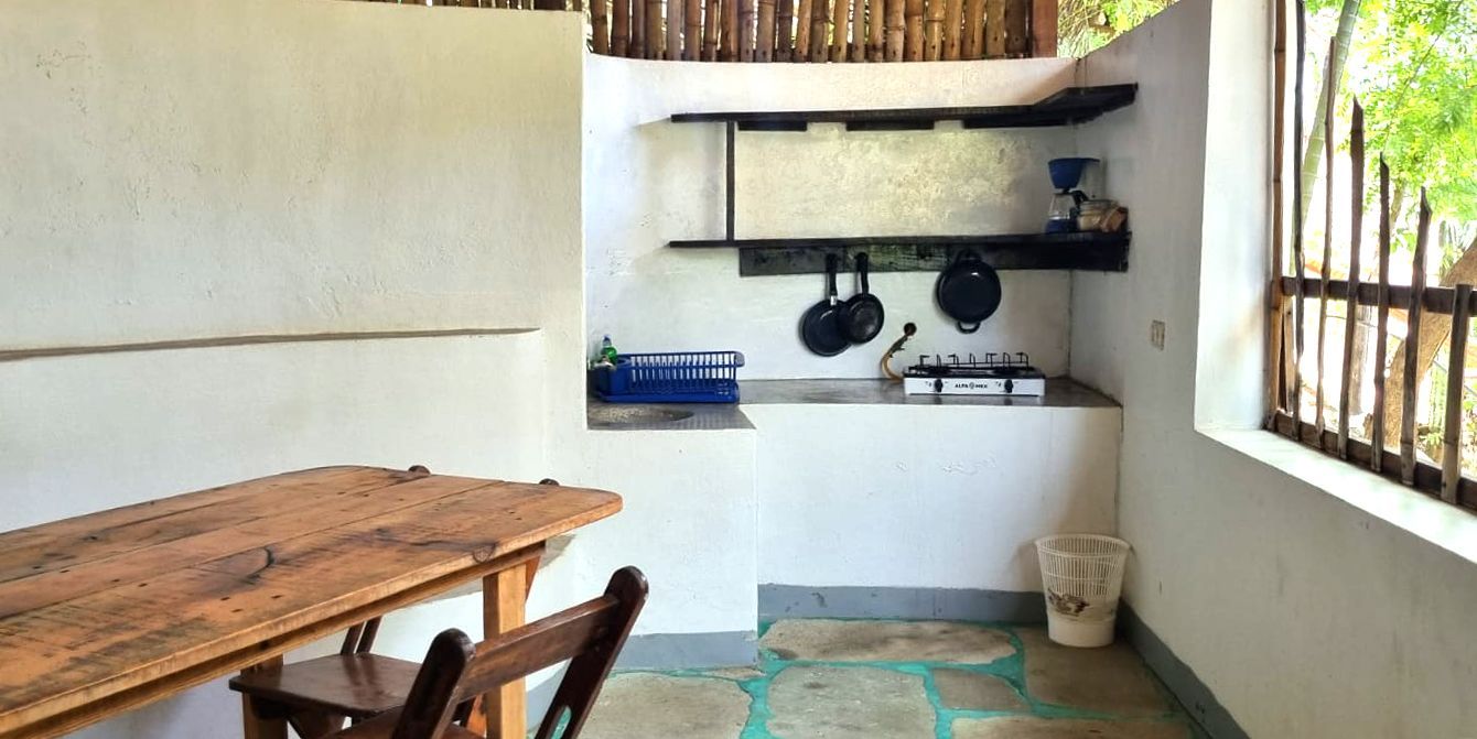 Cocina exterior con mesa de madera, placa de cocina y estantes en posada del arquitecto en mazunte, oaxaca