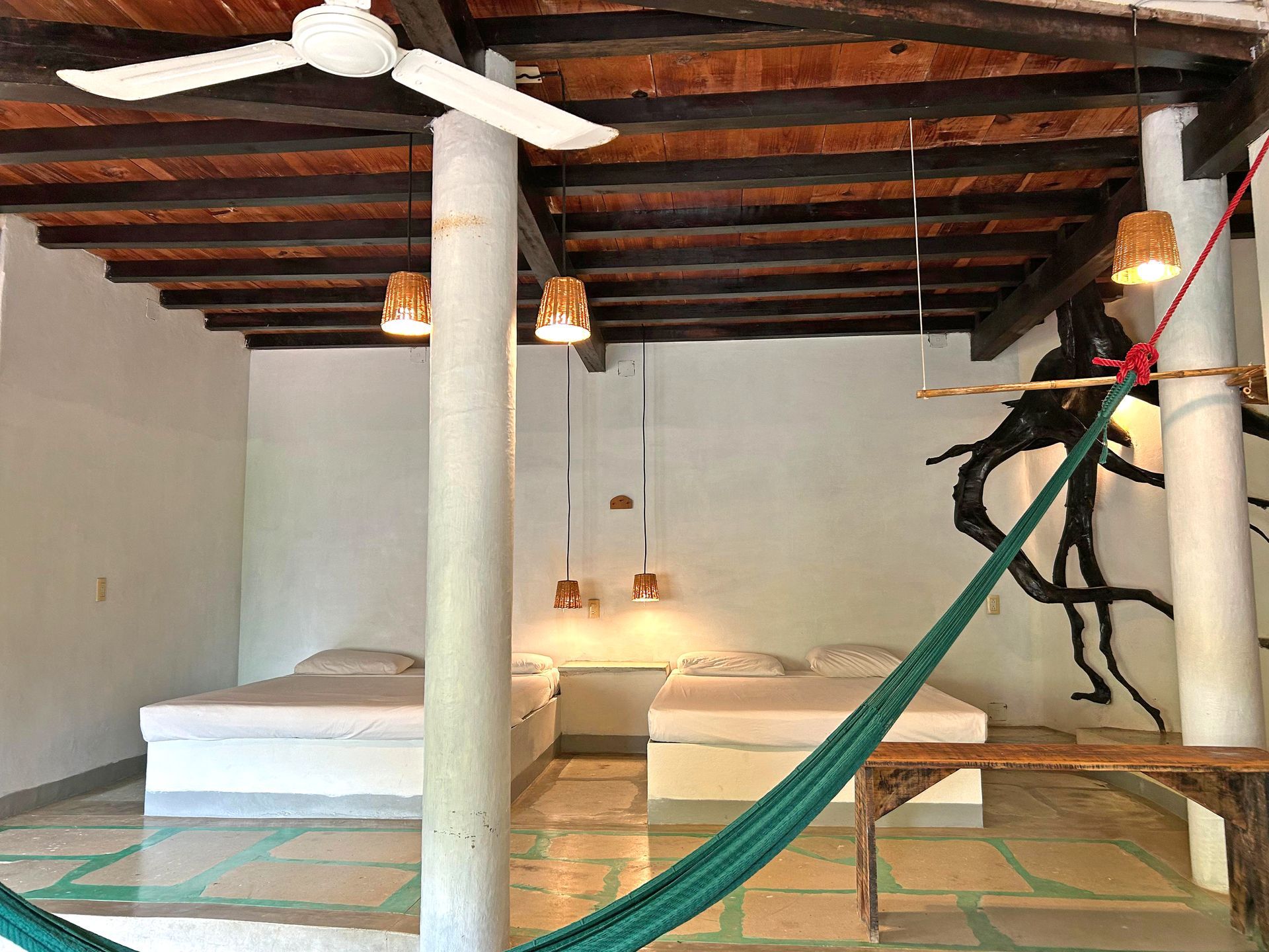 Dormitorio con dos camas, hamaca y raíces de árbol decorativas en posada del arquitecto en mazunte, oaxaca