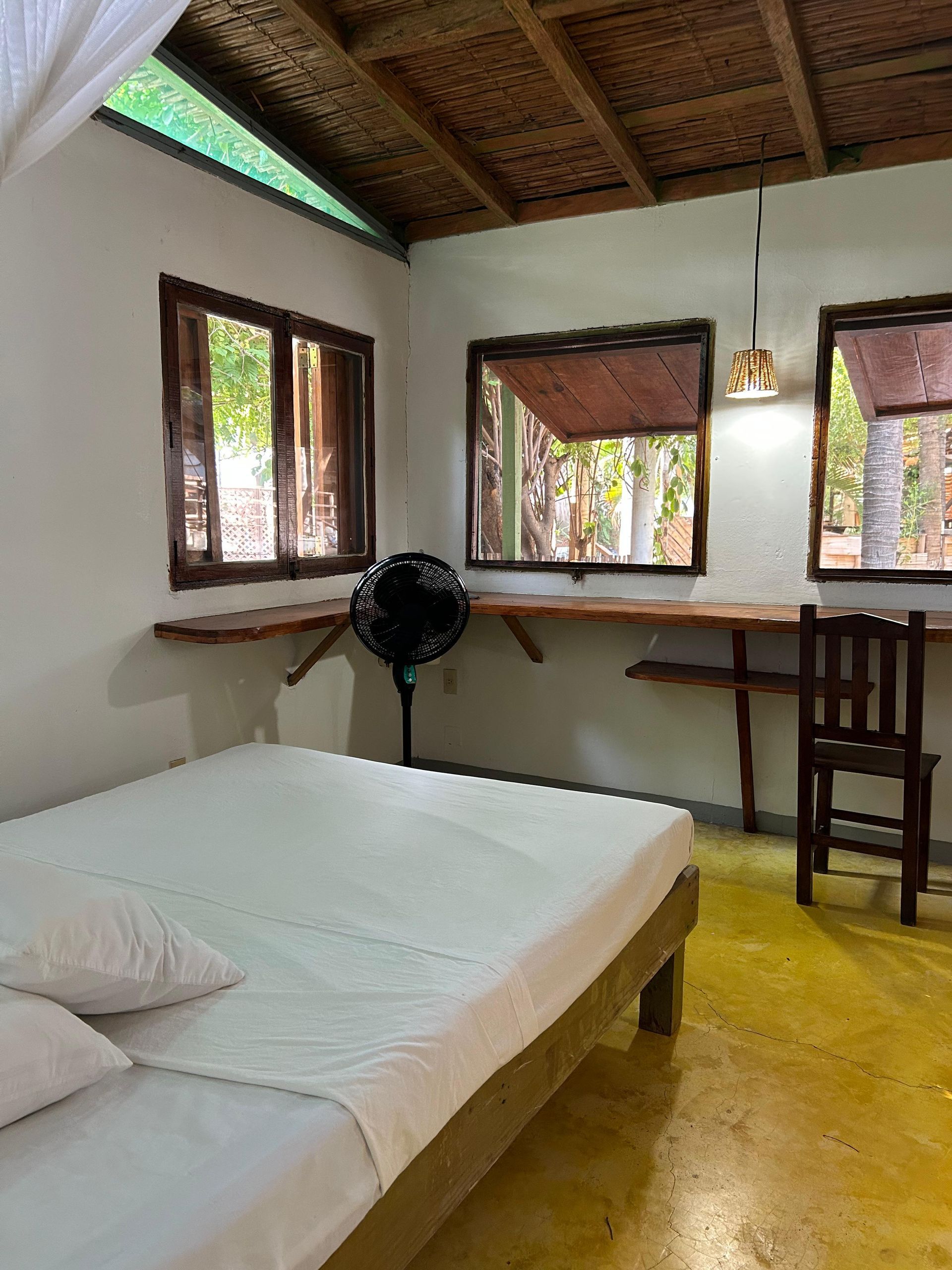 Dormitorio con muebles de madera, ventanas y un ventilador negro en posada del arquitecto en mazunte, oaxaca